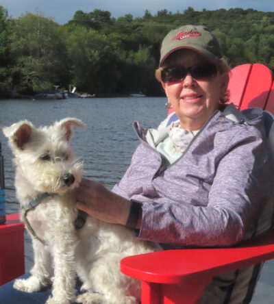 Karen sitting on a red arinondack chair with a small white dog